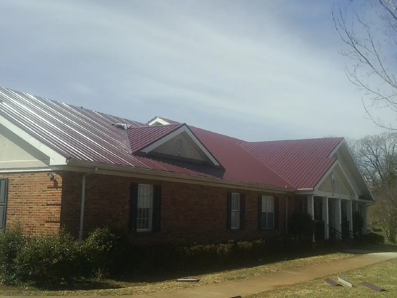 Red metal roof with gabled entries on a long brick building, from a Hail Damage Roof Repair job in Salley