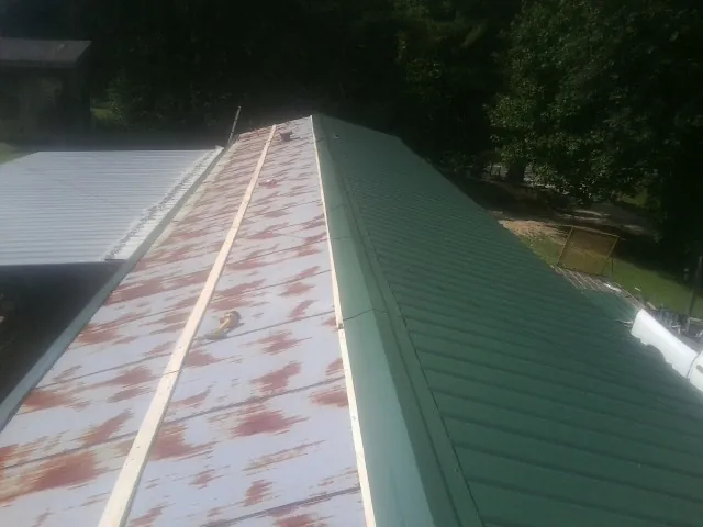 Old rusted panels beside newly installed green metal roofing — Wind Damage Roof Repair by Roofing Brothers in Salley