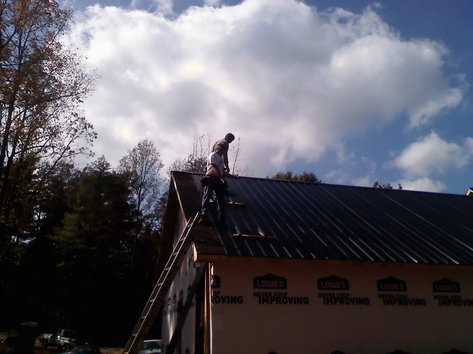 Roofer fastening dark metal panels high against a cloudy sky, from a Roof Inspection job in Salley