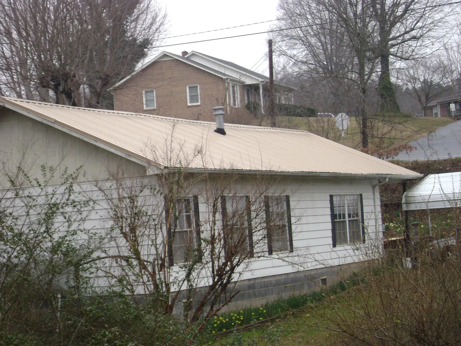 Tan metal roof on a white sided house set into a hillside — Commercial Roofing by Roofing Brothers in Salley